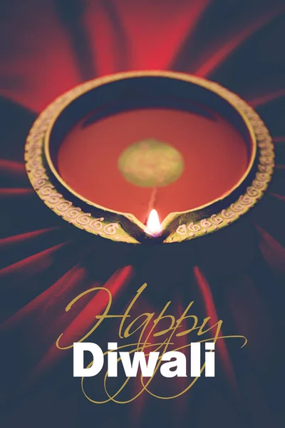 Happy diwali greeting card - Big illuminated diwali diya or clay lamp placed over satin cloth creating rays effect in cloth, moody lighting, selective focus — Stock Photo, Image