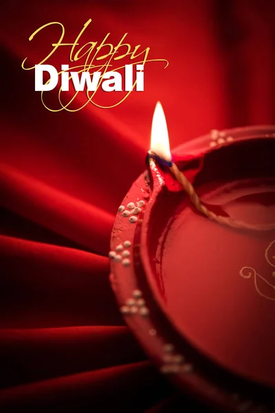 Happy diwali greeting card - Big illuminated diwali diya or clay lamp placed over satin cloth creating rays effect in cloth, moody lighting, selective focus — Stock Photo, Image