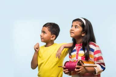Uçurtma veya Hindistan, iki sevimli küçük Hint çocuklar zevk chakri veya ahşap spindal ile ayakta ve heyecan üzerinde mavi arka plan iş parçacığı holding Makar sankranti Festivali, uçan uçurtma uçan Patang
