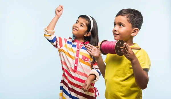 Cometa o Patang volando en la India, dos niños indios lindos disfrutando de Kite volando en el festival de Makar sankranti, de pie con chakri o huso de madera y sosteniendo el hilo en la emoción sobre el fondo azul — Foto de Stock