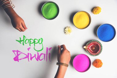 Stock Photo of happy diwali greeting card clicked using elements of Diwali festival like colourful rangoli in bowls, diwali clay lamp or diya and girl or girl making rangoli, writing happy diwali clipart