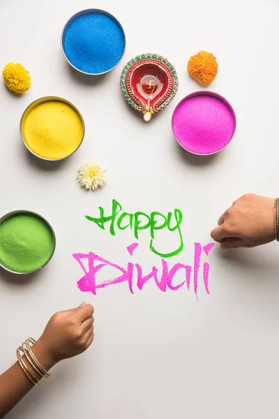 Foto stock de cartão de saudação diwali feliz clicado usando elementos do festival Diwali como rangoli colorido em tigelas, lâmpada de barro diwali ou diya e menina ou menina fazendo rangoli, escrevendo diwali feliz — Fotografia de Stock
