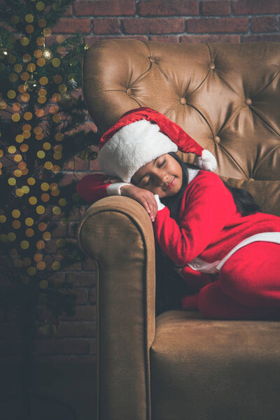 Cute Little Indian or Asian Girl sleeping on chair while waiting for Santa Claus on Christmas night