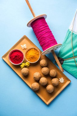 mutlu Makar Sankranti tebrik kartı - Tilgul veya bir kase veya plate haldi Recep ile ve Fikri Reel/Chakri /Spool renkli iplik veya manjha ve düz arka plan üzerinde uçurtma ile çiçeklerle gidecektir Til