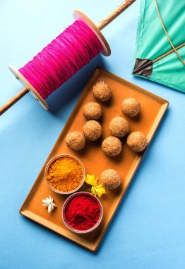 mutlu Makar Sankranti tebrik kartı - Tilgul veya bir kase veya plate haldi Recep ile ve Fikri Reel/Chakri /Spool renkli iplik veya manjha ve düz arka plan üzerinde uçurtma ile çiçeklerle gidecektir Til