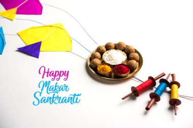 mutlu Makar Sankranti tebrik kartı - Tilgul veya bir kase veya plate haldi Recep ile ve Fikri Reel/Chakri /Spool renkli iplik veya manjha ve düz arka plan üzerinde uçurtma ile çiçeklerle gidecektir Til