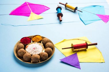 mutlu Makar Sankranti tebrik kartı - Tilgul veya bir kase veya plate haldi Recep ile ve Fikri Reel/Chakri /Spool renkli iplik veya manjha ve düz arka plan üzerinde uçurtma ile çiçeklerle gidecektir Til