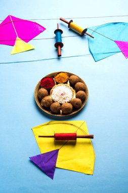 happy Makar Sankranti greeting card - Tilgul or Til ladoo in a bowl or plate with haldi kumkum and flowers with Fikri /Reel/Chakri /Spool with colourful thread or manjha and kite over plain background clipart