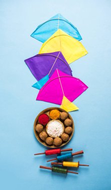 happy Makar Sankranti greeting card - Tilgul or Til ladoo in a bowl or plate with haldi kumkum and flowers with Fikri /Reel/Chakri /Spool with colourful thread or manjha and kite over plain background clipart