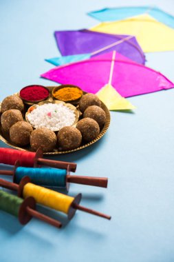 mutlu Makar Sankranti tebrik kartı - Tilgul veya bir kase veya plate haldi Recep ile ve Fikri Reel/Chakri /Spool renkli iplik veya manjha ve düz arka plan üzerinde uçurtma ile çiçeklerle gidecektir Til