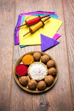 mutlu Makar Sankranti tebrik kartı - Tilgul veya bir kase veya plate haldi Recep ile ve Fikri Reel/Chakri /Spool renkli iplik veya manjha ve düz arka plan üzerinde uçurtma ile çiçeklerle gidecektir Til