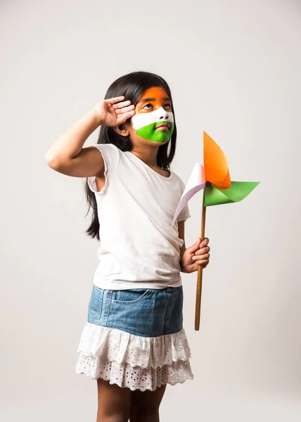 indian girl with paper windmill toy made up of tricolour or indian flag colours. Saluting, looking at camera or with red heart toy, celebrating 26 January republic day or 15 august independence day