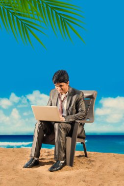 Hintli işadamı rahatlatıcı plajda soğuk içecekler veya dizüstü, plaj topu, telefonda konuşurken veya el ile yayıldı