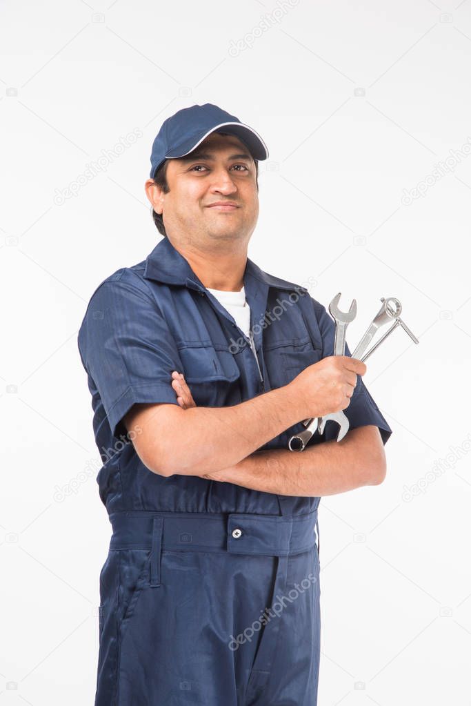 Indian happy auto mechanic in blue suit and cap holding spanner tool in action, isolated over white background