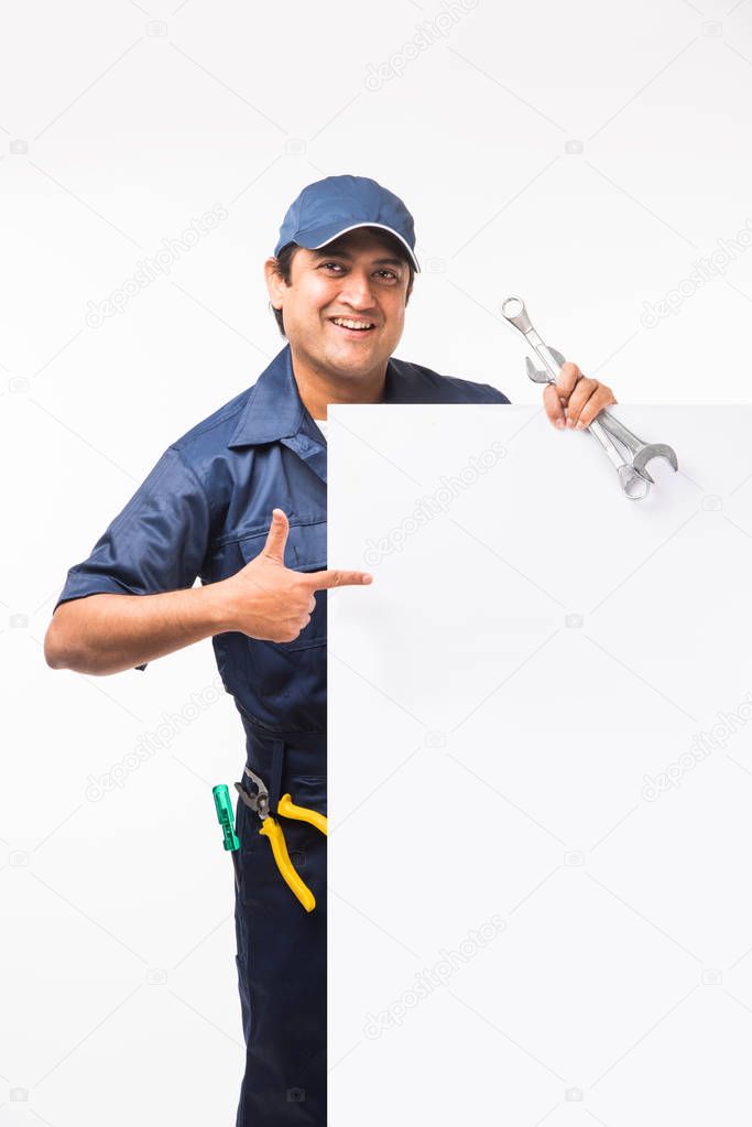 Indian happy auto mechanic in blue suit and cap holding spanner tool in action, isolated over white background