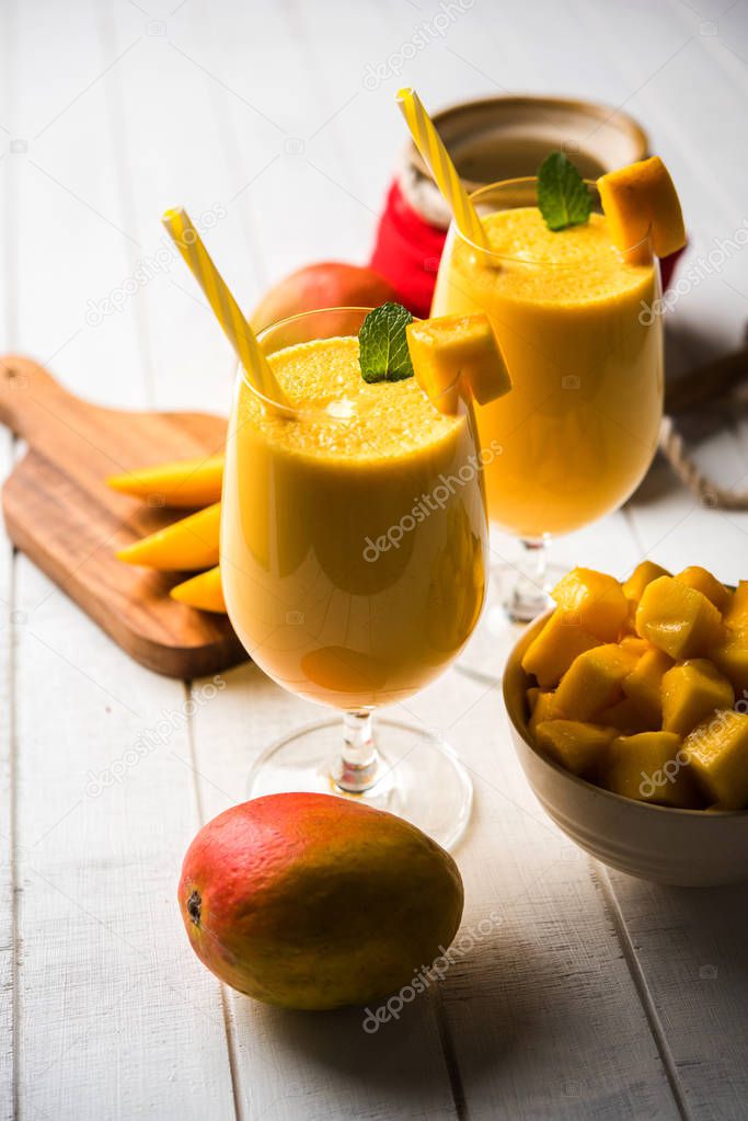 Mango Lassi or smoothie in big glasses with curd, cut fruit pieces and blender