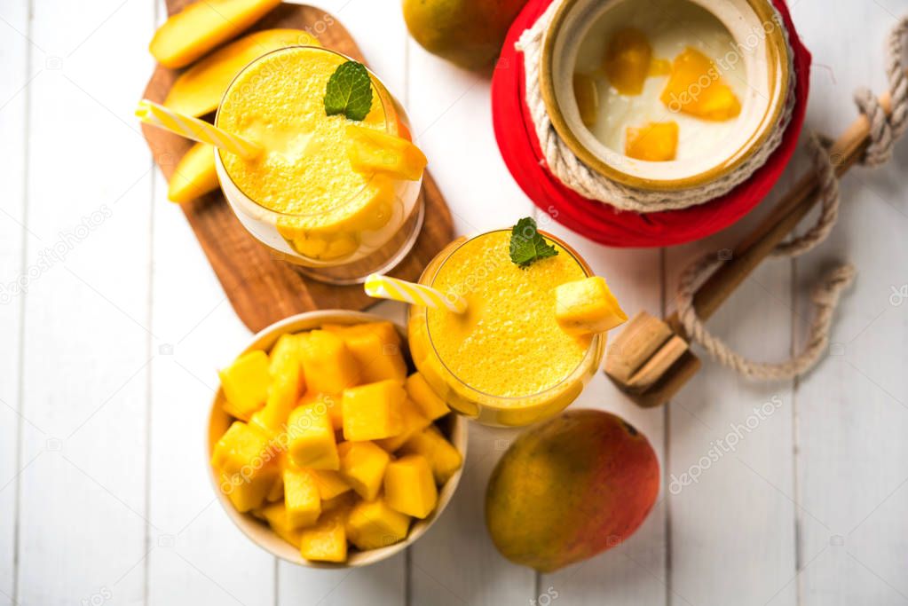 Mango Lassi or smoothie in big glasses with curd, cut fruit pieces and blender