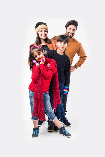 Studio portrait of happy Indian family in warm clothes standing against white background. Ready for winter concept