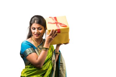 Sari giymiş Hintli bir kadın elinde hediye kutusuyla beyaz arka planda dikiliyor.