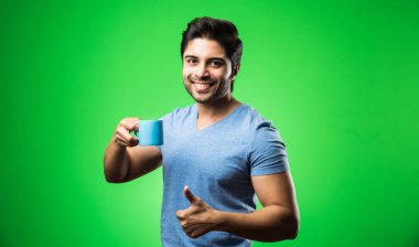 Çay fincanı ya da kupası olan Hintli bir adam. Yeşil arka planda tek başına dikilirken içmek, sunmak veya tutmak