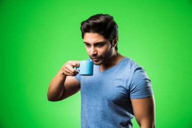 Çay fincanı ya da kupası olan Hintli bir adam. Yeşil arka planda tek başına dikilirken içmek, sunmak veya tutmak
