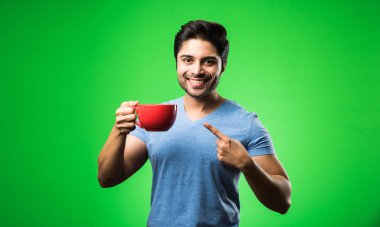 Çay fincanı ya da kupası olan Hintli bir adam. Yeşil arka planda tek başına dikilirken içmek, sunmak veya tutmak