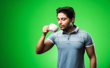 Çay fincanı ya da kupası olan Hintli bir adam. Yeşil arka planda tek başına dikilirken içmek, sunmak veya tutmak