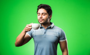 Çay fincanı ya da kupası olan Hintli bir adam. Yeşil arka planda tek başına dikilirken içmek, sunmak veya tutmak