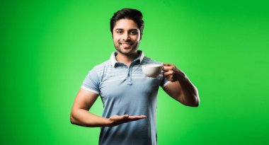 Çay fincanı ya da kupası olan Hintli bir adam. Yeşil arka planda tek başına dikilirken içmek, sunmak veya tutmak