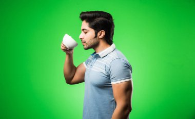 Çay fincanı ya da kupası olan Hintli bir adam. Yeşil arka planda tek başına dikilirken içmek, sunmak veya tutmak