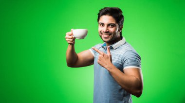 Çay fincanı ya da kupası olan Hintli bir adam. Yeşil arka planda tek başına dikilirken içmek, sunmak veya tutmak