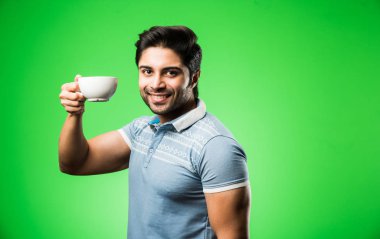 Çay fincanı ya da kupası olan Hintli bir adam. Yeşil arka planda tek başına dikilirken içmek, sunmak veya tutmak