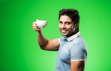 Çay fincanı ya da kupası olan Hintli bir adam. Yeşil arka planda tek başına dikilirken içmek, sunmak veya tutmak