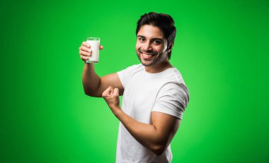 Hintli bir adam yeşil arka planda tek başına dikilirken sütü bardağa dolduruyor.