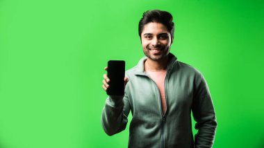 Akıllı telefonlu Hintli ya da Asyalı adam yeşil arka planda tek başına duruyor.