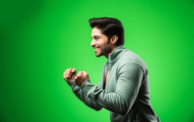 Başarı jestli yakışıklı Hintli adam, yeşil arka planda tek başına duruyor.