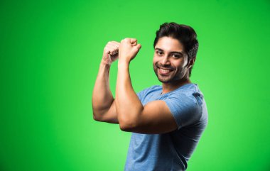 Başarı jestli yakışıklı Hintli adam, yeşil arka planda tek başına duruyor.