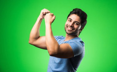 Başarı jestli yakışıklı Hintli adam, yeşil arka planda tek başına duruyor.