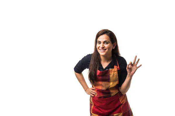 Portrait of Indian woman chef or cook in apron, presenting, pointing, with ok sign, thumbs up or hands folded. standing isolated over white background