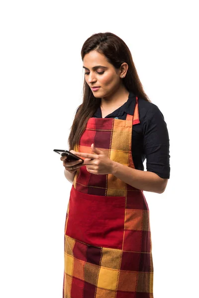 Indian woman / female chef in apron using smartphone while standing isolated over white background