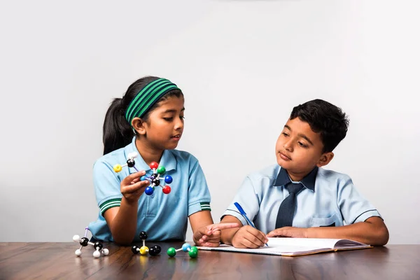 Indian school boy and girl or science student in uniform Using Molecular Model Kit for studying physics, selective focus