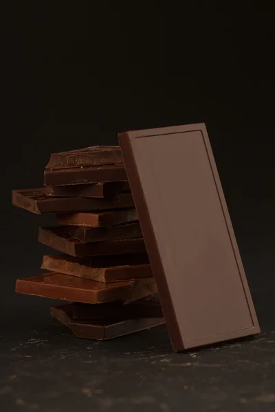 Quadrado em forma de pedaços de chocolate no fundo escuro — Fotografia de Stock