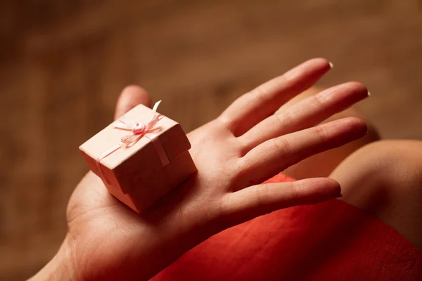 Mão aberta de uma mulher segurando uma pequena caixa de presente rosa — Fotografia de Stock