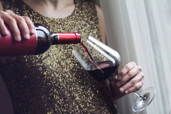 woman with gold spangle dress pouring red wine into a glass