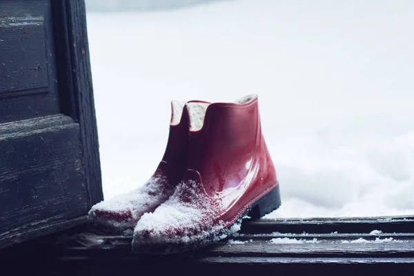Röd gummi skor täckt av snö vid dörren — Stockfoto