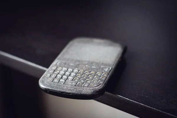 Старий смартфон з пилом на чорній полиці — стокове фото
