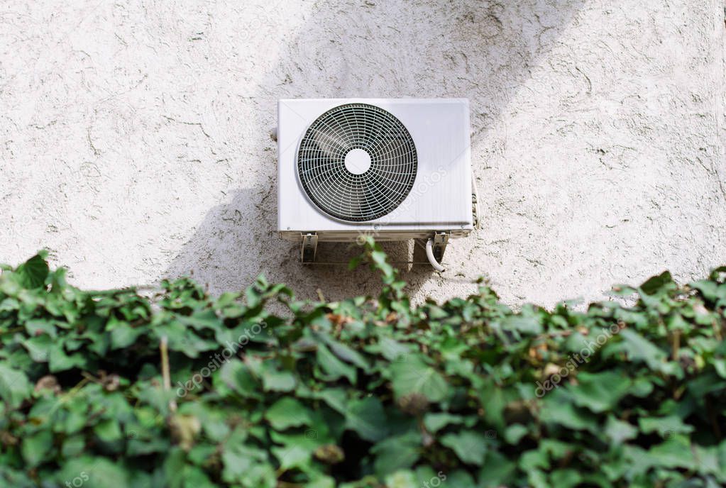 air conditioning unit behind a green leaves wall