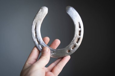 Ön görüntüde, beyaz adamın eli, gri arka planda parlak, çelikten, parlak, parlak, parlak bir boynuzlu ayakkabı tutuyor. 
