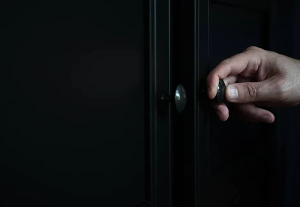 perspective side view closeup of Caucasian man hand opening a wooden closed black clothes dresser cabinet with a metallic door knob