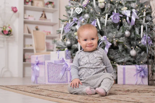 Noel ağacı önünde oturan neşeli bebek kız